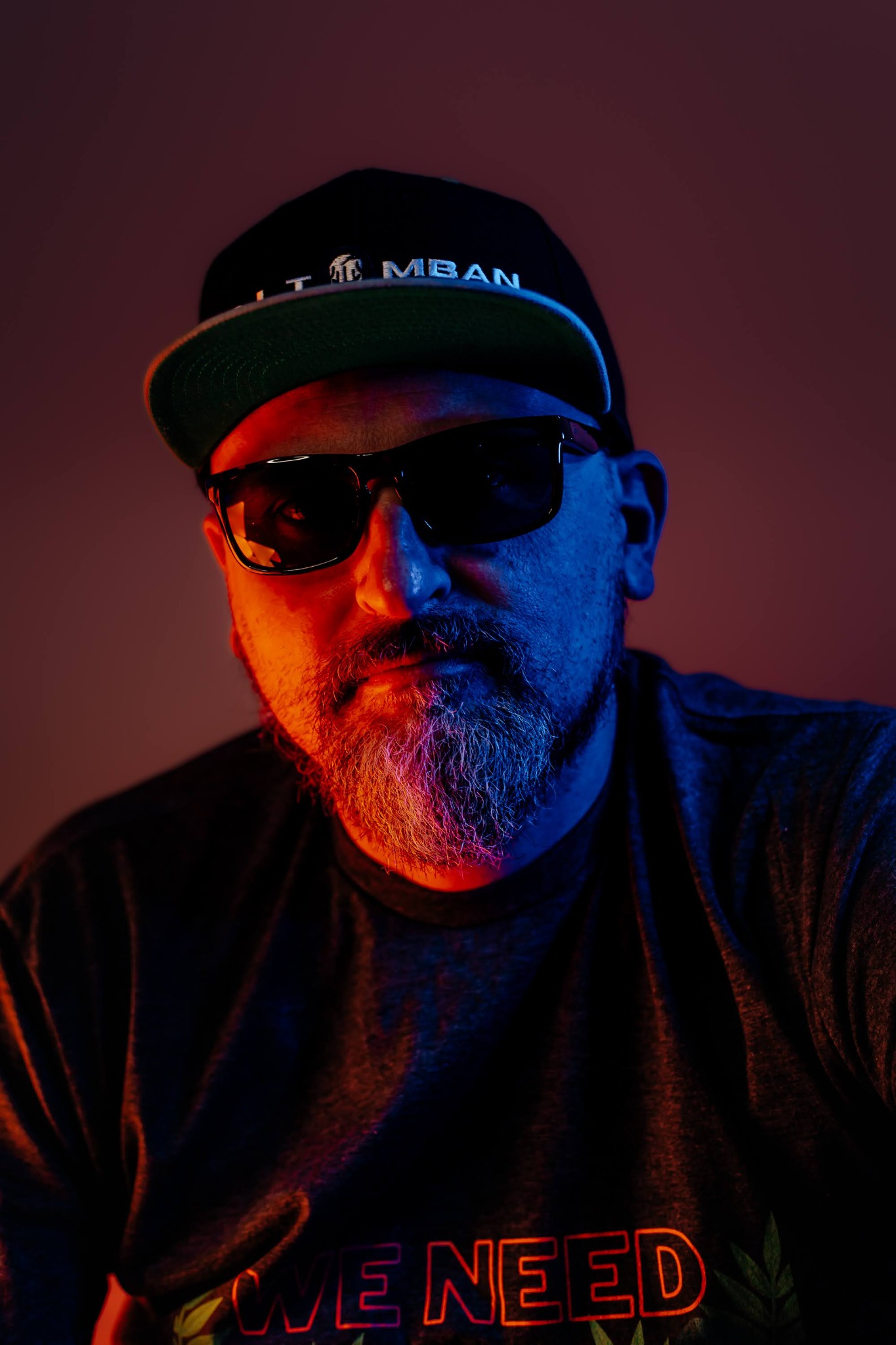 DJ Tomban in a cap and sunglasses, lit in red and blue